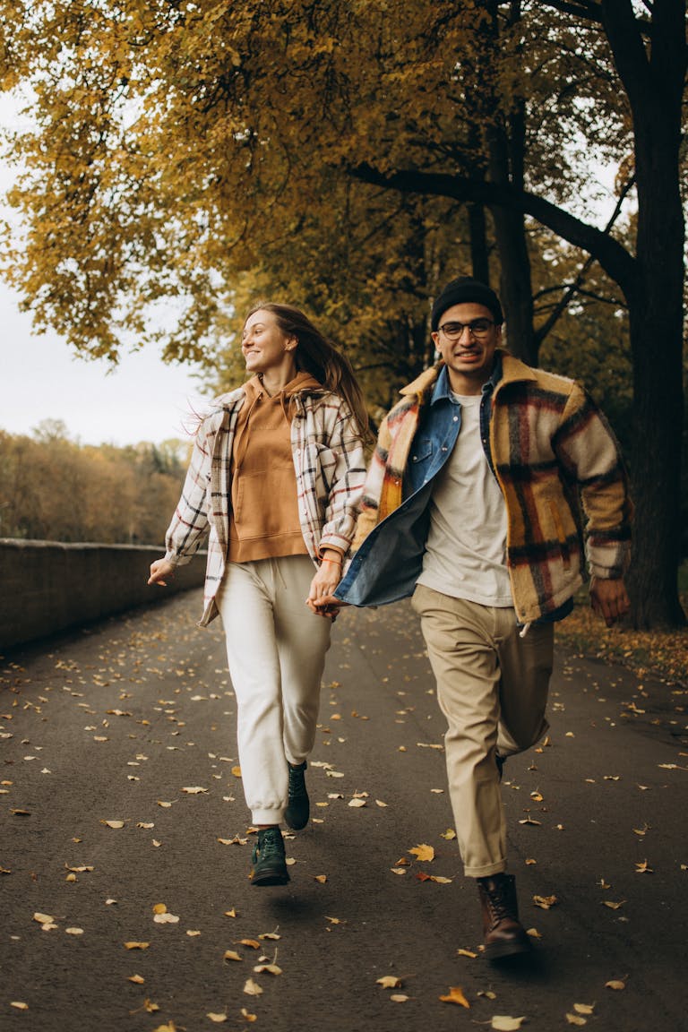 A joyful couple running hand in hand through a scenic autumn park.