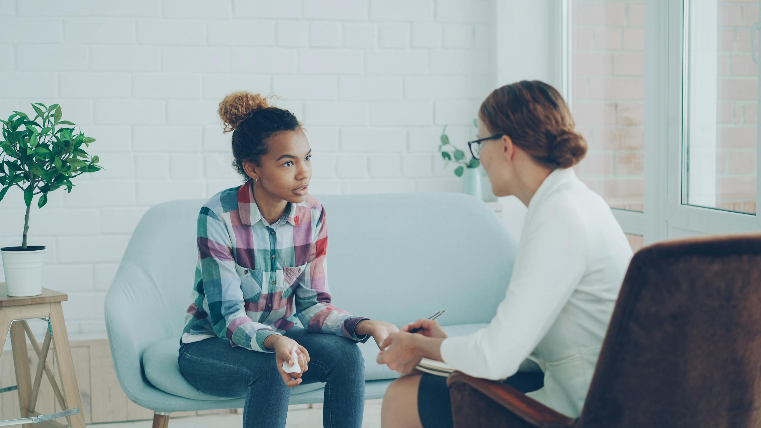 A teenager and therapist having a counseling session in a bright, modern office setting.