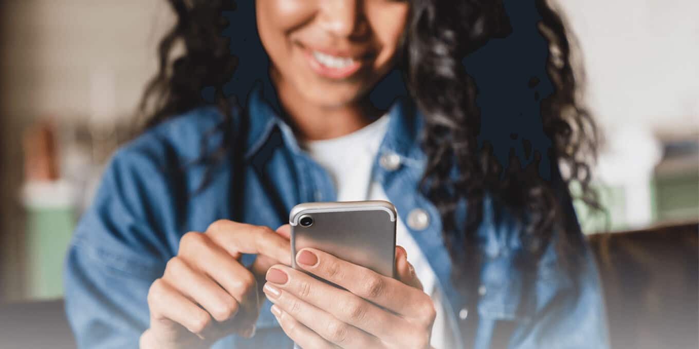 A person in a denim jacket smiles while using a smartphone.