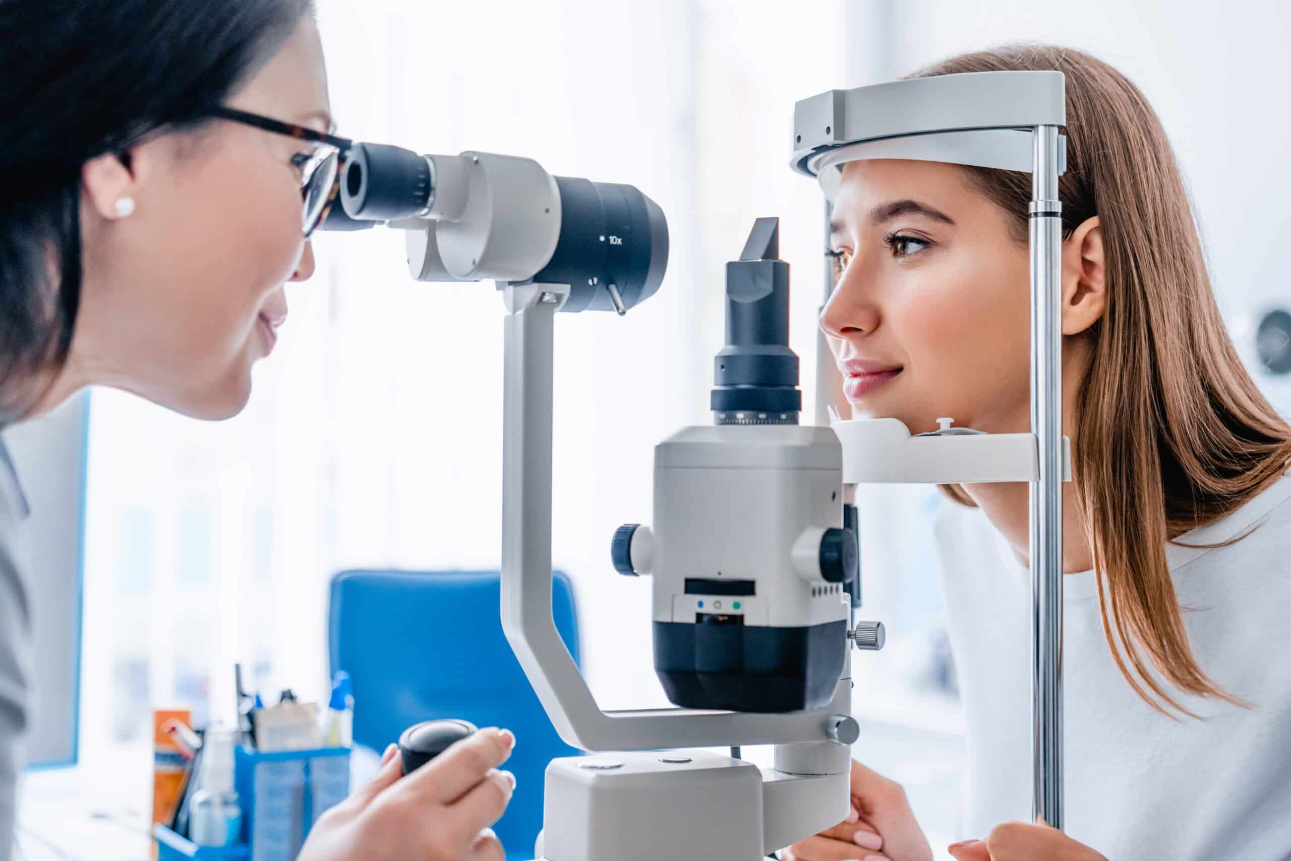 An optometrist examines a patient's eyes using a slit lamp in a bright clinic. The atmosphere is professional and focused on eye care.