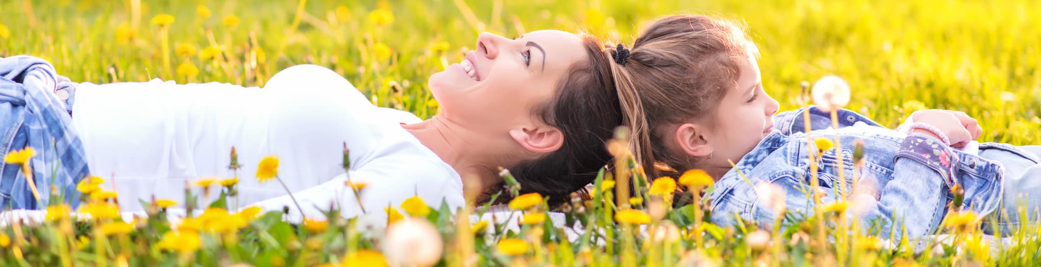A woman and child lie smiling in a vibrant meadow filled with yellow flowers, bathed in warm sunlight, conveying joy and tranquility.